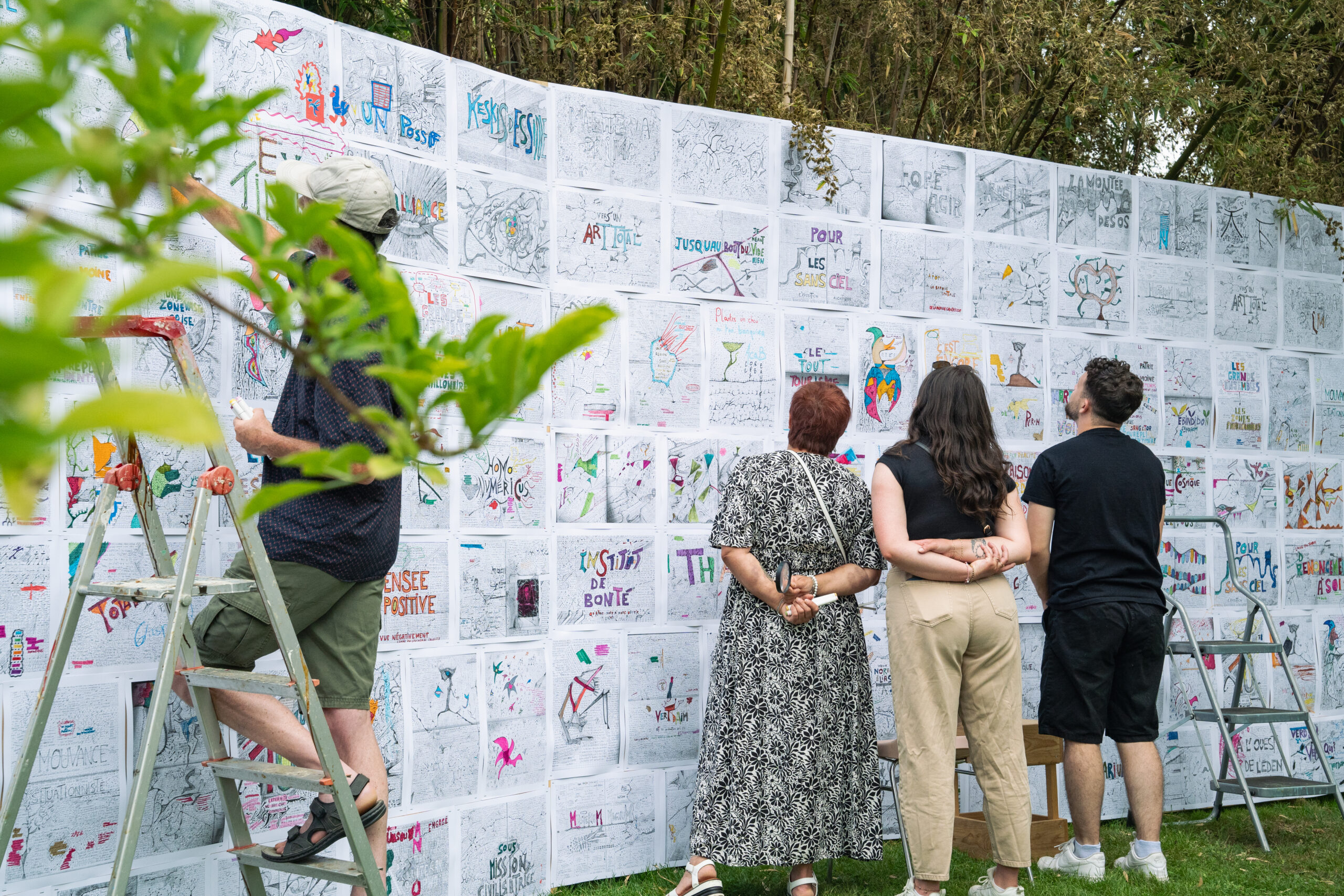 Un groupe de festivaliers observe attentivement une exposition artistique installée dans le parc de la Roseraie pendant le festival Les Entrelacés, mettant en valeur la dimension culturelle et immersive de l’événement.