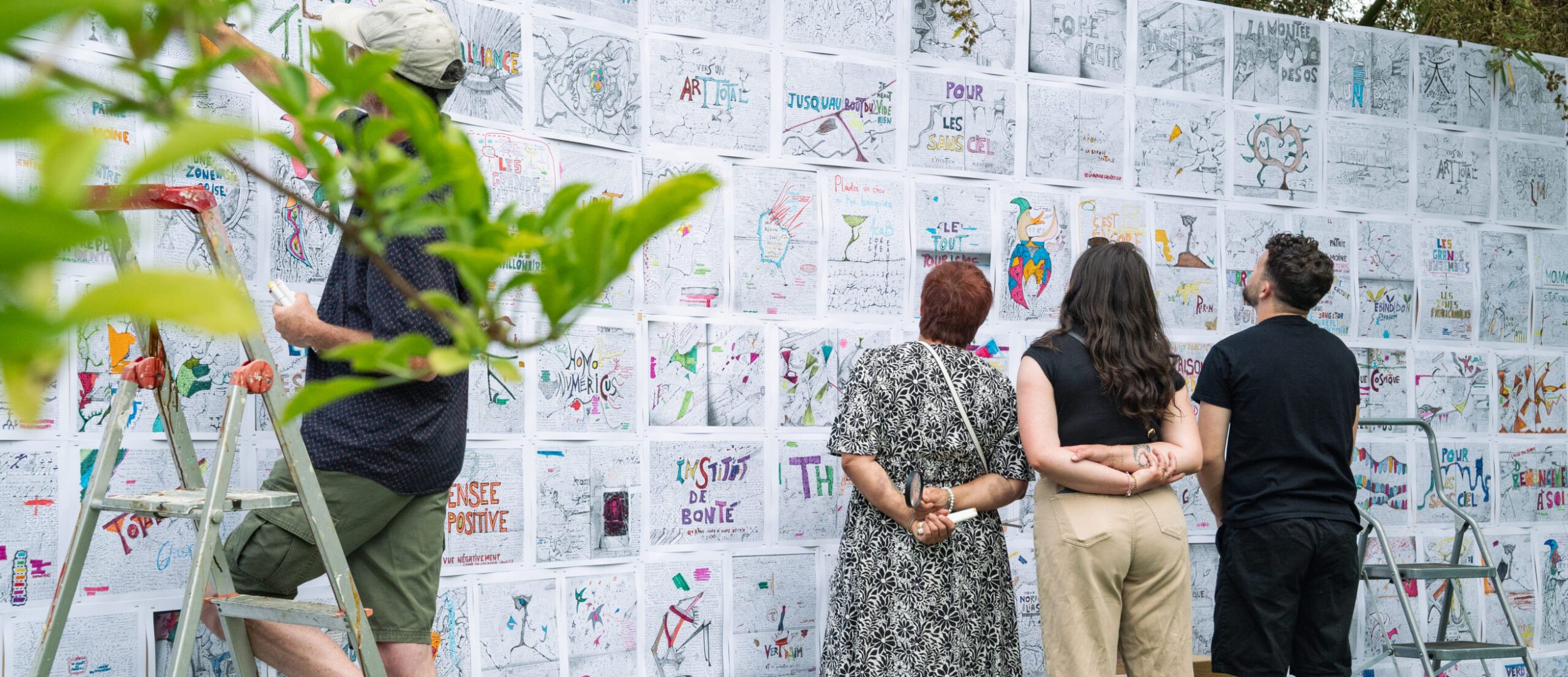 Un groupe de festivaliers observe attentivement une exposition artistique installée dans le parc de la Roseraie pendant le festival Les Entrelacés, mettant en valeur la dimension culturelle et immersive de l’événement.